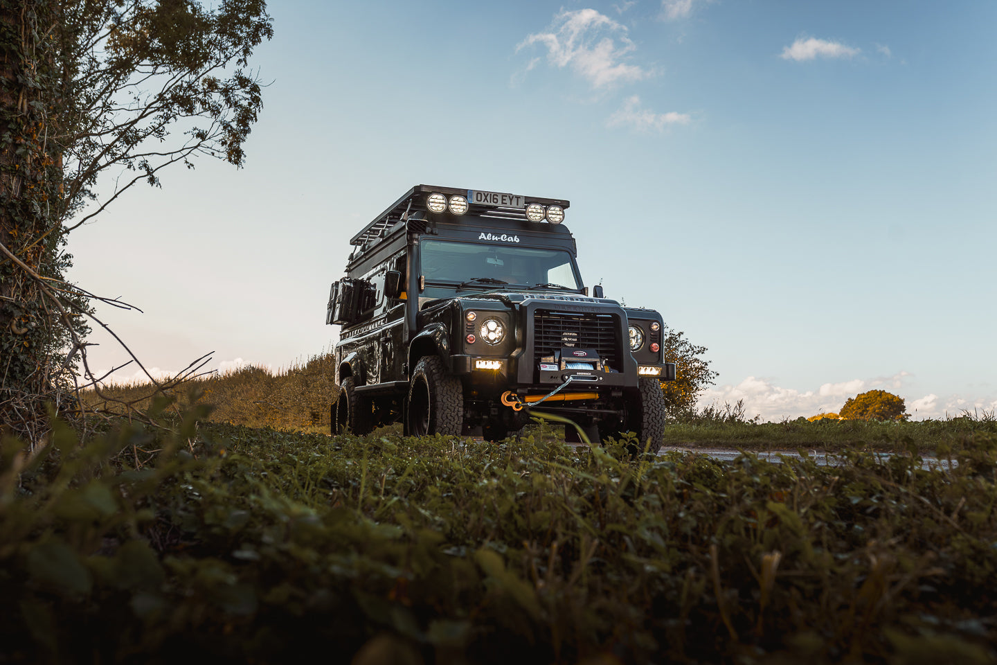 Land Rover Defender in a natural setting with trees and open sky.